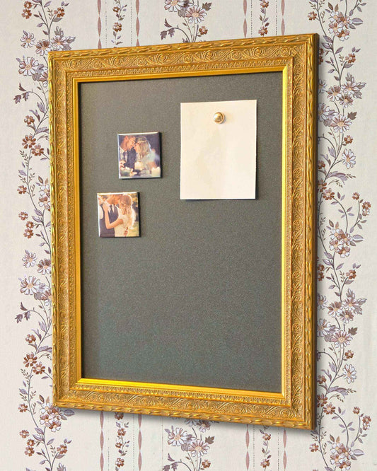 Gold framed magnetic board on a floral wallpaper wall with small photo magnets and a pinned note, styled as a decorative home memo board.