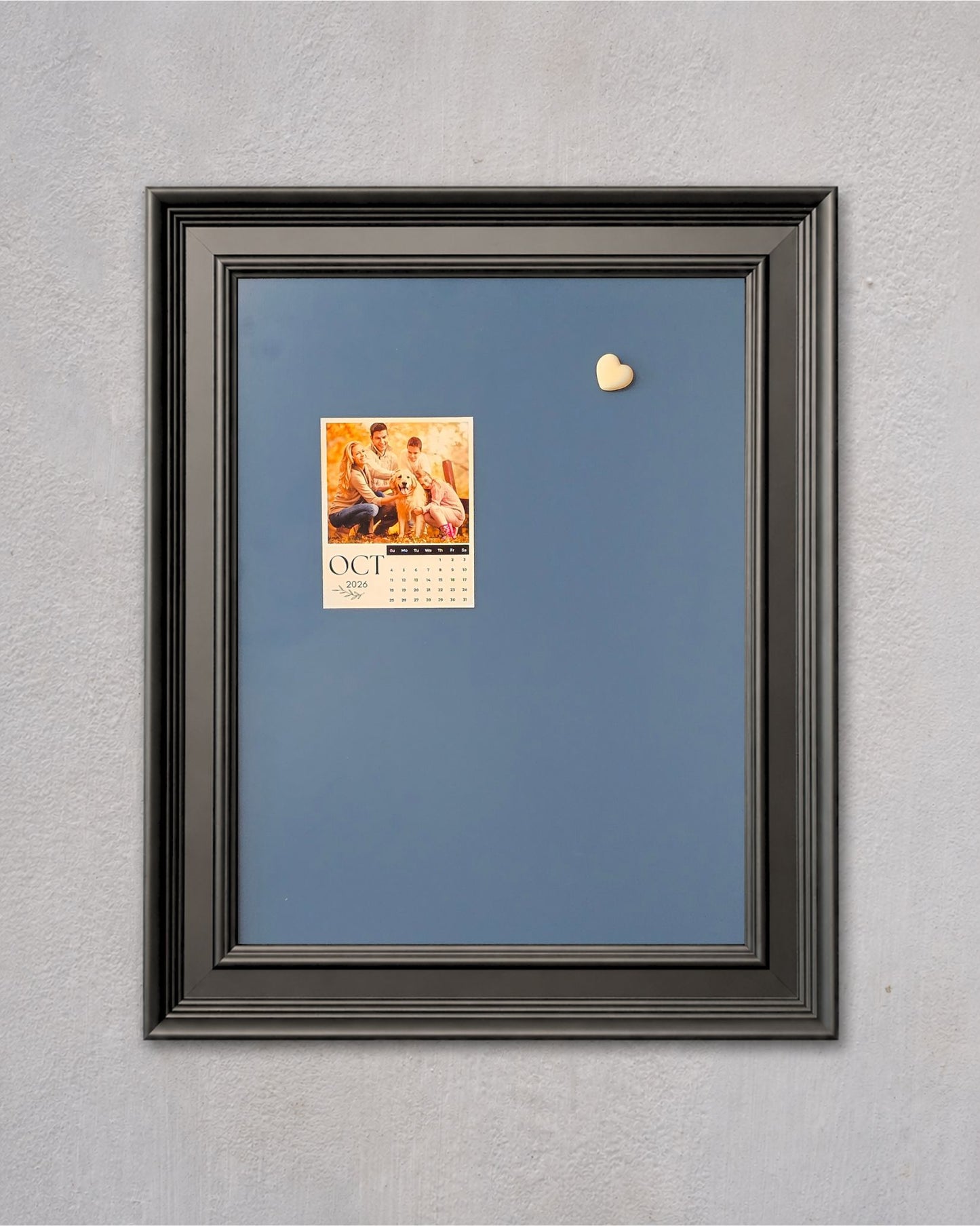 Blue magnetic memo board with a modern black solid wood frame displaying a mini calendar and decorative heart magnet on a textured gray wall.