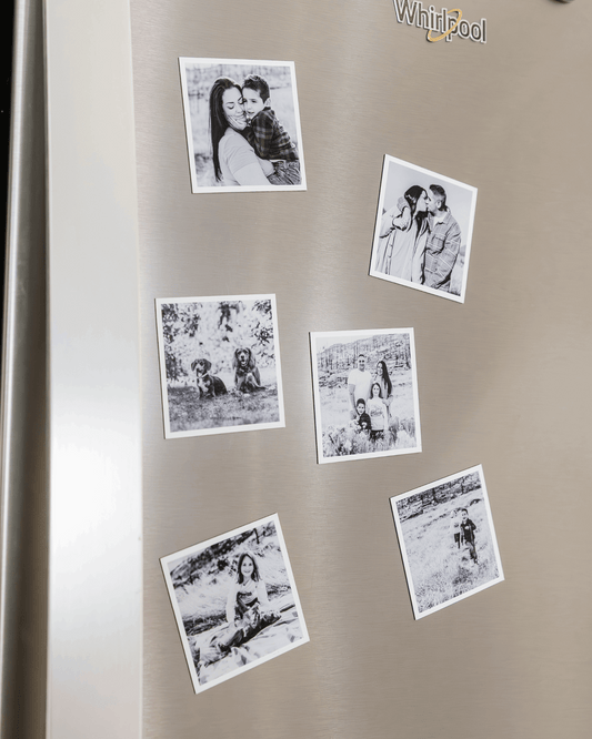 Black and white custom photo magnets displayed on a stainless steel refrigerator door.