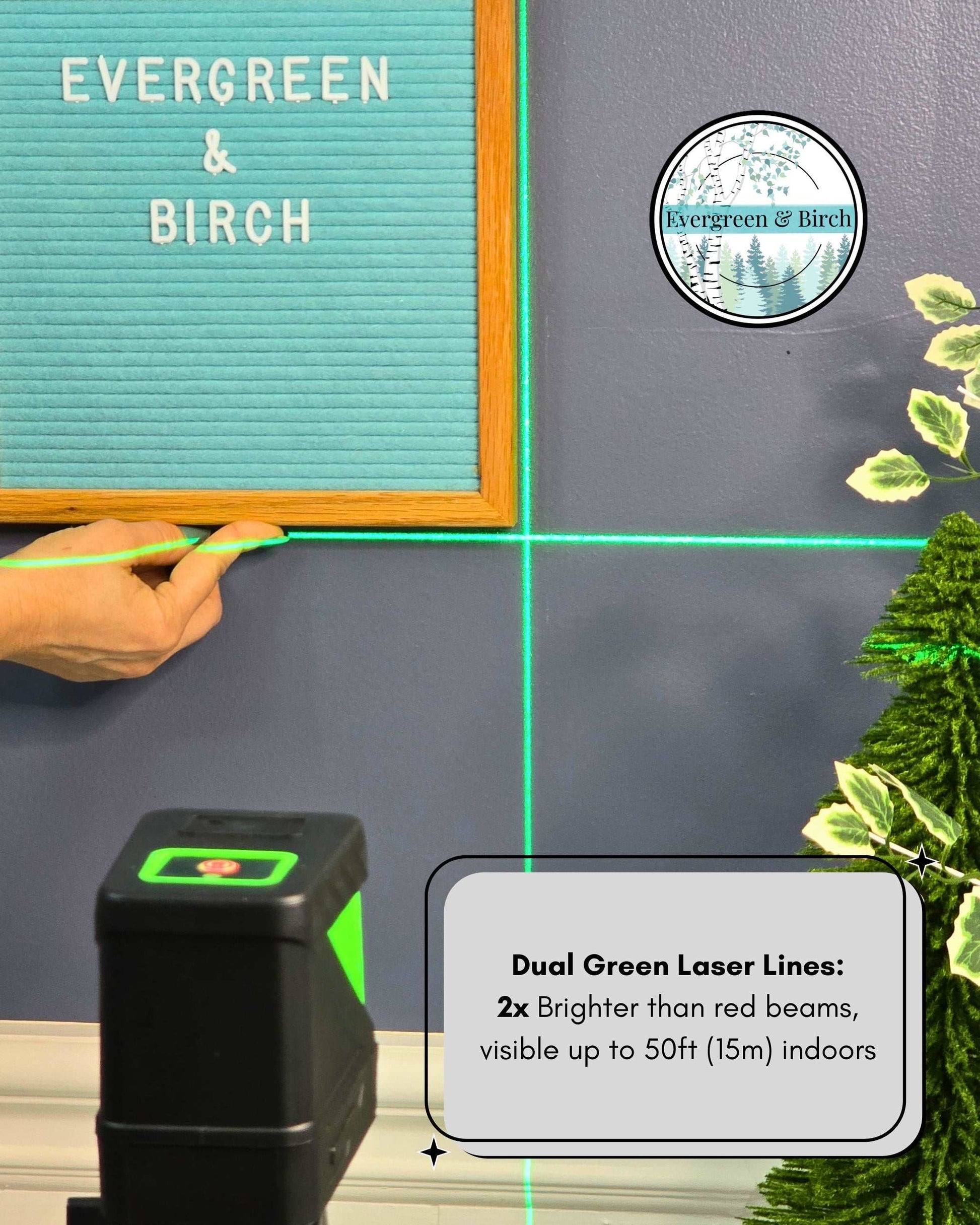 Green cross-line laser level projecting vertical and horizontal beams to align gallery wall frame for perfect picture hanging.