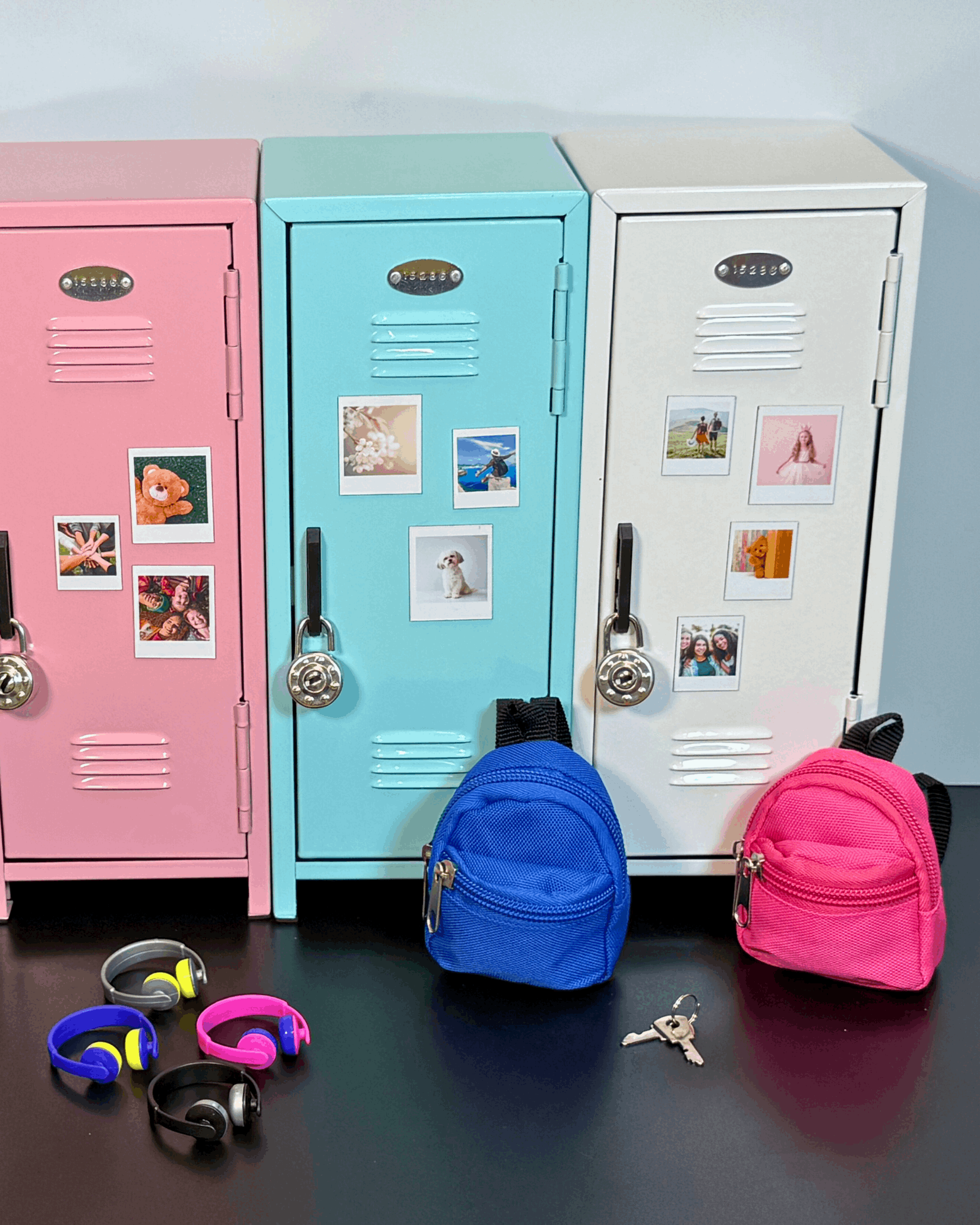 Mini retro metal lockers in pink, blue, and white with photo magnets, styled as a kids desk organizer with mini backpacks and accessories.