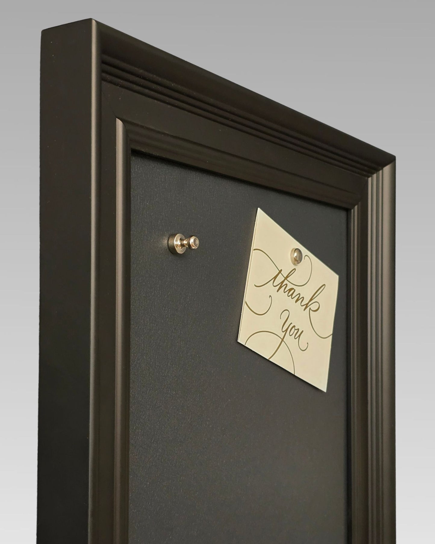 Angled close-up of a modern black magnetic board with solid pine wood frame, featuring a magnetic note holder and textured powder-coated steel surface.