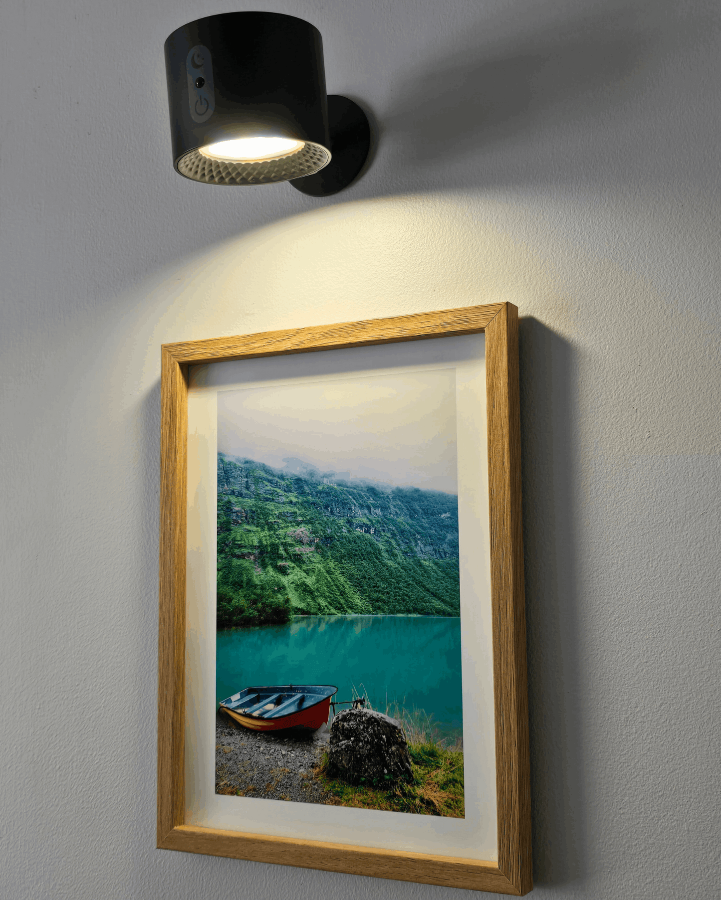 Framed landscape photo of a lake with mountains, illuminated by a wall-mounted black light fixture.