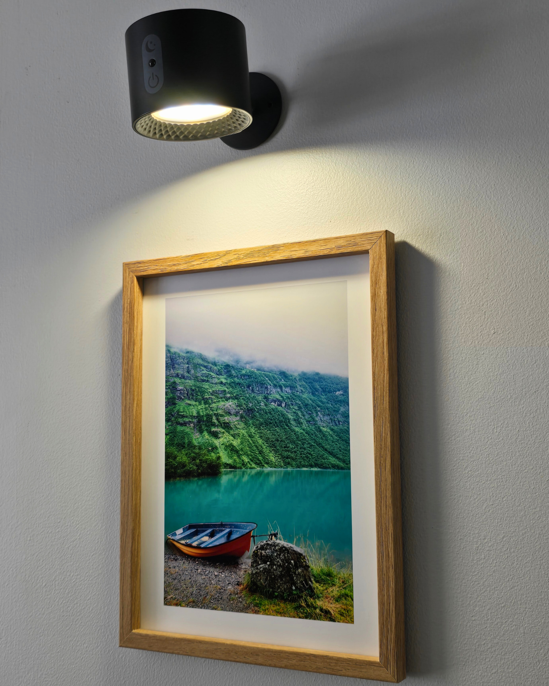 Framed landscape photo of a lake with mountains, illuminated by a wall-mounted black light fixture.