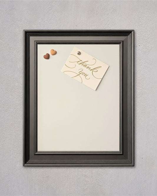 Modern black magnetic board with white powder-coated steel surface, featuring a pinned thank you note and decorative heart magnets on a textured gray wall.